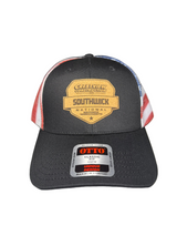 A black trucker hat with a curved brim, featuring a tan and black 'Southwick National' shield logo on the front. The back panels have a red, white, and blue striped pattern.